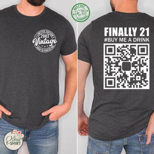 May include: Dark gray t-shirt with white text and graphics. The front features a circular design that reads "Limited Edition 2003 Vintage Aged to Perfection." The back says "Finally 21 #BUY ME A DRINK" with a QR code.