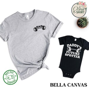 Pu&ograve; includere: Un set di due t-shirt, una grigia e una nera. La t-shirt grigia ha la scritta "DAD" e un grafico di bilanciere. La t-shirt nera ha il testo "DADDY'S FUTURE SPOTTER" e un grafico di bilanciere.
