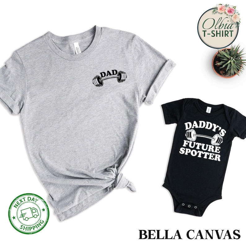 Pu&ograve; includere: Un set di due t-shirt, una grigia e una nera. La t-shirt grigia ha la scritta "DAD" e un grafico di bilanciere. La t-shirt nera ha il testo "DADDY'S FUTURE SPOTTER" e un grafico di bilanciere.