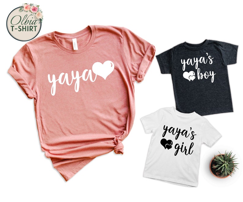 K&ouml;nnte beinhalten: Drei T-Shirts mit einem Herzen und dem Text "yaya's". Das gr&ouml;&szlig;te Shirt ist rosa und sagt "yaya" mit einem Herzen. Die kleineren Shirts sind schwarz und wei&szlig; und sagen "yaya's boy" und "yaya's girl" mit Herzen.