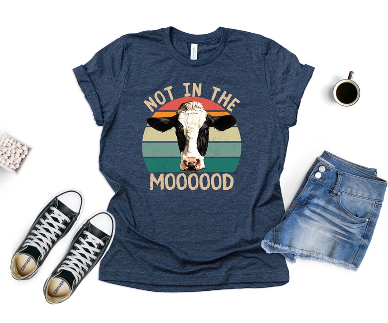 May include: A navy blue t-shirt with a retro-style graphic of a cow's head in front of a sunset. The text "Not in the Mooooood" is printed below the graphic.