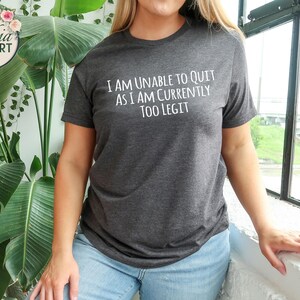 May include: A dark gray t-shirt with the text "I am unable to quit as I am currently too legit" printed in white.