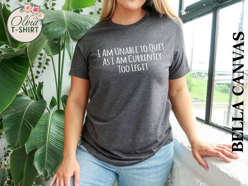 May include: A dark gray t-shirt with the text "I am unable to quit as I am currently too legit" printed in white.