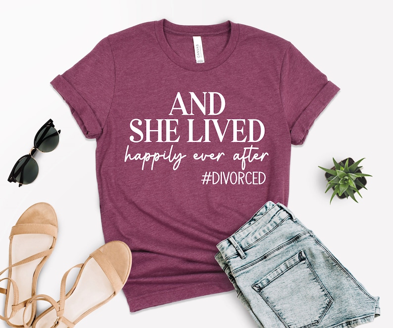 Puede incluir: Una camiseta color granate con el texto "AND SHE LIVED happily ever after #DIVORCED" en blanco.