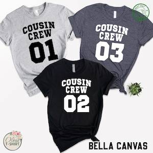 K&ouml;nnte beinhalten: Drei T-Shirts mit dem Text "COUSIN CREW" und den Zahlen 01, 02 und 03 in fetter, wei&szlig;er Schrift. Die Shirts sind grau, schwarz und marineblau. Der Markenname "BELLA CANVAS" ist schwarz gedruckt.