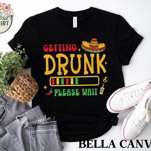 May include: Black t-shirt with a graphic of a sombrero, a progress bar, and the text "Getting Drunk - Please Wait".