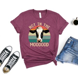May include: A maroon t-shirt with a vintage-style graphic of a cow's head with the text "Not in the Mooooood".