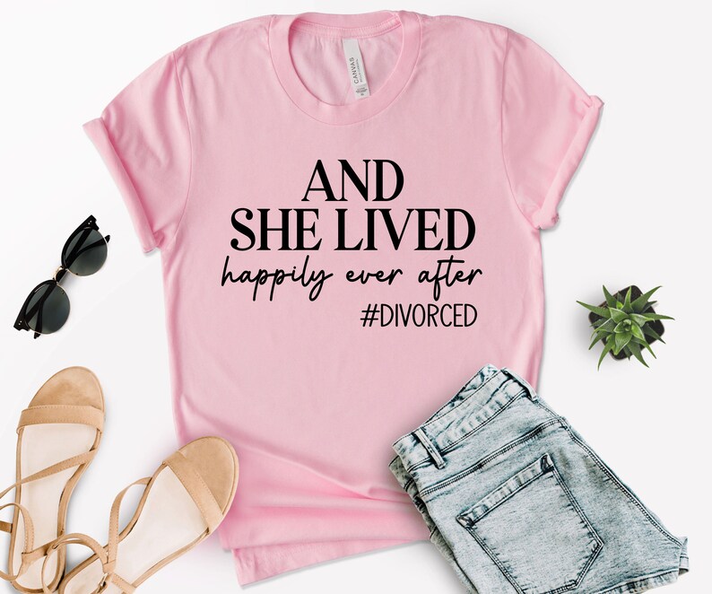 Puede incluir: Camiseta rosa con el texto "AND SHE LIVED happily ever after #DIVORCED" en negro.