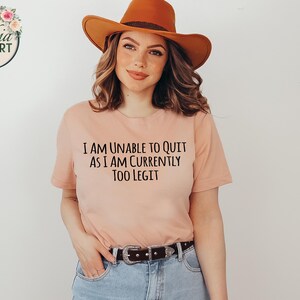 May include: A peach-colored t-shirt with the text "I am unable to quit as I am currently too legit" printed in black.