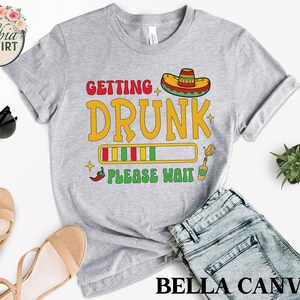 May include: Gray t-shirt with a progress bar graphic that says "Getting Drunk Please Wait". The graphic also includes a sombrero, a chili pepper, and a bottle of alcohol.