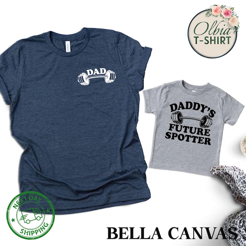 Pu&ograve; includere: Due magliette, una blu navy e una grigia, con un tema di sollevamento pesi. La maglietta blu navy dice "DAD" con un bilanciere e pesi. La maglietta grigia dice "DADDY'S FUTURE SPOTTER" con un bilanciere e pesi.