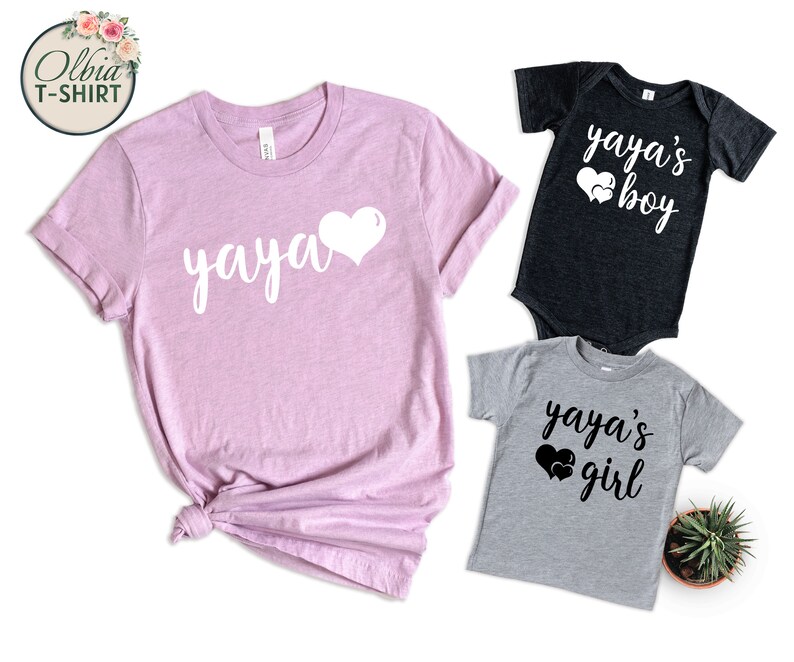 K&ouml;nnte beinhalten: Ein Set aus drei T-Shirts mit dem Text "yaya" und Herzen. Das T-Shirt f&uuml;r Erwachsene ist rosa, das T-Shirt f&uuml;r Jungen ist schwarz und das T-Shirt f&uuml;r M&auml;dchen ist grau.