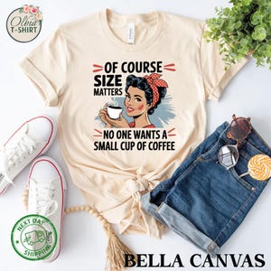 May include: A beige t-shirt with a graphic of a woman holding a cup of coffee. The text on the shirt reads "Of course size matters. No one wants a small cup of coffee."