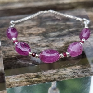 May include: A silver chain bracelet with five oval-shaped pink gemstones and small silver beads.