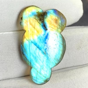 Può includere: Una pietra preziosa di labradorite lucidata intagliata in una forma organica arrotondata. La pietra mostra una vibrante iridescenza con evidenti bagliori di blu elettrico e giallo dorato sulla sua superficie liscia e riflettente.