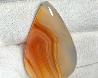 May include: A teardrop-shaped pendant made of agate with orange, yellow, and white banding.
