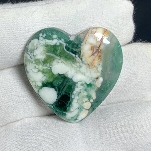 Peut inclure: Une pierre d'agate en forme de cœur de couleur verte et blanche avec un motif tourbillonnant. La pierre est polie et a une surface lisse.