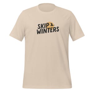 Könnte beinhalten: Ein beiges T-Shirt mit einem schwarzen grafischen Aufdruck, der "SKIP WINTERS" mit einem stilisierten Sonnen- und Vogeldesign sagt.