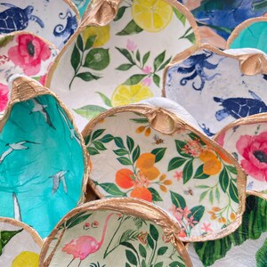 May include: A collection of decorative bowls made from seashells, each with a different colorful and patterned design. The bowls feature various themes, including tropical plants, lemons, birds, and sea turtles.