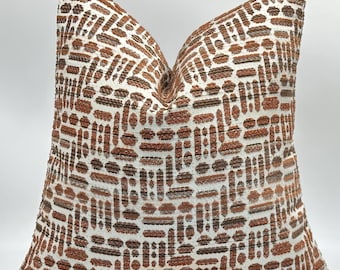 May include: A decorative throw pillow with a geometric pattern in shades of brown and white. The pillow features a repeating design of rectangular and oval shapes, creating a textured appearance. The pillow is designed to add a decorative touch to any room.