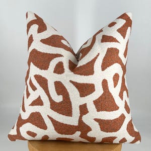 May include: A white and orange throw pillow with an abstract pattern. The pillow is made of a soft, textured fabric.
