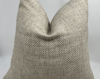 May include: A beige throw pillow with a textured woven fabric. The pillow is square shaped and has a subtle sheen.