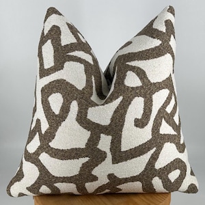 May include: A white and brown patterned throw pillow with a geometric design. The pillow is made of a soft, textured fabric.
