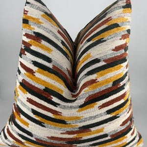 May include: A decorative throw pillow with a white background and a striped pattern in shades of brown, green, and yellow.