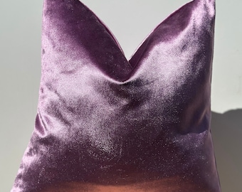 May include: A soft, plush cushion with a light purple velvet cover. The cushion is square shaped and has a subtle sheen.