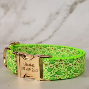 Op de afbeelding: Een groene en gouden hondenriem met een herhalend avocado-patroon. De riem heeft een gouden gesp met de naam "Chester" en het telefoonnummer "321-889-7523" erop gegraveerd.
