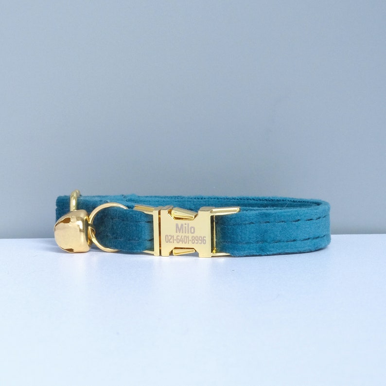 Puede incluir: Collar de terciopelo azul turquesa para gato con hebilla dorada y cascabel. La hebilla tiene el nombre "Milo" y el n&uacute;mero de tel&eacute;fono "021-5401-8996" grabados.