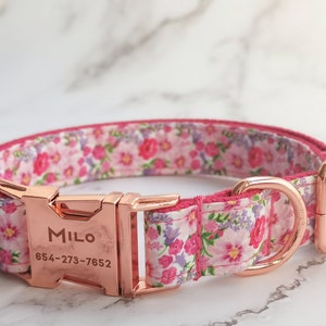 May include: A pink floral dog collar with a rose gold buckle and D-ring. The buckle is engraved with the name "Milo" and the phone number "654-273-7652".