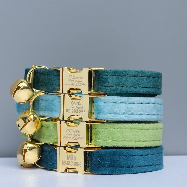 Puede incluir: Cuatro collares de terciopelo para gatos en azul verdoso, azul claro, verde y azul verdoso con hebillas y cascabeles dorados. Cada hebilla tiene un nombre y un n&uacute;mero de tel&eacute;fono personalizados. Los nombres son Chester, Stella, Stella y Milo.