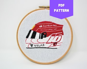 May include: Embroidered design of a red and white race car helmet with the text "Santander", "#essereFerrari", and "VELAS" on it. The design is in a wooden embroidery hoop.