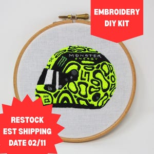 May include: An embroidery hoop containing white fabric with a stitched design of a racing helmet in neon yellow and black. The helmet features the Monster Energy logo and text. The text EMBROIDERY DIY KIT is visible in the upper right corner.