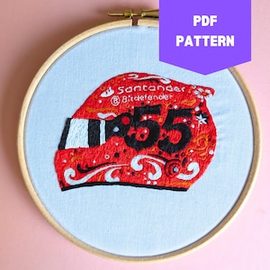 May include: Embroidered design of a red racing helmet with the number 55, white and black stripes, and the text "Santander & Bitdefender". The design is on a light blue fabric, framed in a wooden hoop. A purple banner reads "PDF PATTERN".