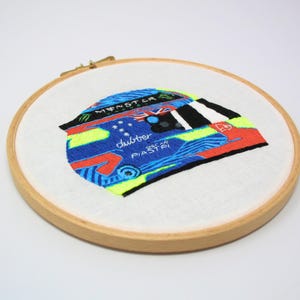 May include: Embroidered design of a racing helmet with a blue, red, yellow and black colour scheme. The helmet has the words "Monster" and "Piastri" on it.