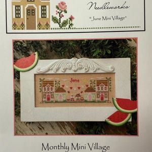 Op de afbeelding: Een kruissteekpatroon getiteld "June Mini Village" met twee huizen, een banner met de tekst "June" en decoratieve watermeloenschijfjes. De tekst "Country Cottage Needleworks" is ook zichtbaar.