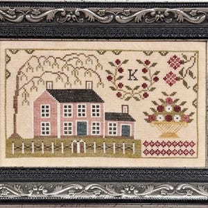 Könnte beinhalten: Eine Kreuzstich-Stickerei, die ein rosa Haus mit grünem Dach und weißen Verzierungen zeigt, umgeben von einer Trauerweide und einem Blumenkorb. Die Stickerei ist in einem schwarzen und silbernen Rahmen gerahmt und enthält den Buchstaben "K" in der oberen rechten Ecke.