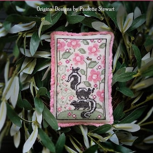 Può includere: Un sampler a punto croce con una famiglia di puzzole in mezzo a fiori rosa e verde, con il testo "Stench Stack" e "Plum Street Samplers". Il disegno è incorniciato con un bordo rosa.