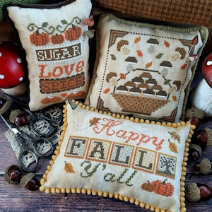 Puede incluir: Tres fundas de cojín bordadas con diseños de otoño. La primera funda de cojín es beige con costuras marrones y el texto "Sugar, Love, Spice". La segunda funda de cojín es beige con costuras marrones y una cesta de setas. La tercera funda de cojín es beige con costuras marrones y el texto "Happy Fall Y'all".