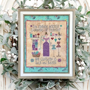 Puede incluir: Un bordado de punto de cruz enmarcado con una mujer con un vestido morado y un gato. El texto dice "She maketh herself coverings of tapestry. Her clothing is silk and purple."