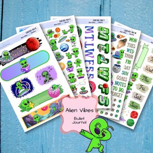 May include: A collection of colorful alien-themed stickers for bullet journals. The stickers feature green aliens, planets, and space-themed elements. The text "Alien Vibes" and "Bullet Journal" are visible. The stickers are arranged on a blue wooden surface.