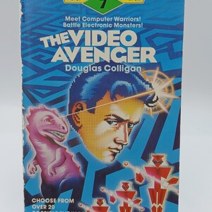 Peut inclure: Un livre de poche vintage intitulé "The Video Avenger" de Douglas Colligan. La couverture présente une illustration stylisée d'un visage d'homme avec un faisceau laser, un dinosaure rose et des figures de robots rouges. Le livre fait partie de la série Twistaplot.