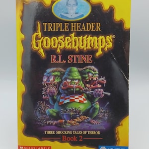 May include: A paperback book titled "Triple Header Goosebumps" by R.L. Stine. The cover features a grotesque green creature with a red and white checkered bib, holding a spoon. The book is Book 2 in the series, with the Scholastic and Parachute logos.