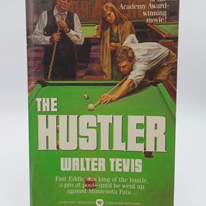 May include: Vintage paperback book cover for "The Hustler" by Walter Tevis. The cover features a green pool table with a player aiming, and illustrations of other characters. Text includes the title and author.