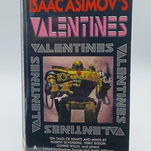 May include: A vintage paperback book titled "Isaac Asimov's Valentines." The cover features a yellow robot holding a rose, with the title in pink and the author's name in white. The book is a collection of science fiction stories.