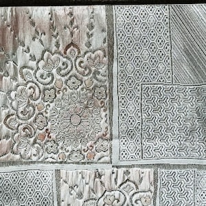 May include: A close-up of a silver and gray patterned wallpaper with a repeating geometric design. The wallpaper has a textured surface and a subtle sheen.