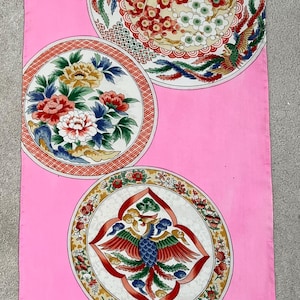 May include: A pink textile with a repeating pattern of circular designs. Each circle features a central motif of a phoenix or floral arrangement, surrounded by intricate details in red, yellow, green, and blue.