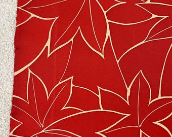 May include: Close-up of red fabric featuring a repeating pattern of cream-coloured stylized leaves. The leaves are maple-leaf shaped with prominent veins. The fabric is next to a white, textured surface.